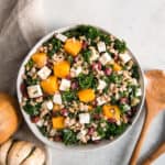 butternut squash kale salad in bowl next to wooden serving utensils.