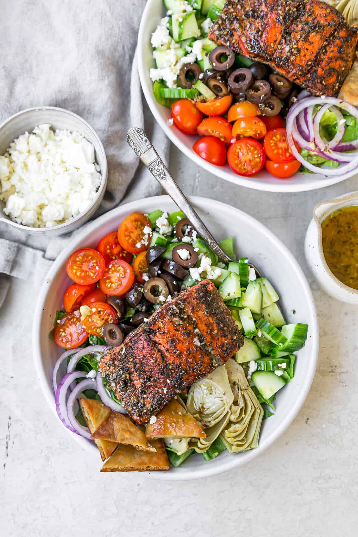 two servings of greek salmon salad in bowls with silver fork