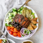 greek salmon salad in bowls with fork next to linen and dressing bowl