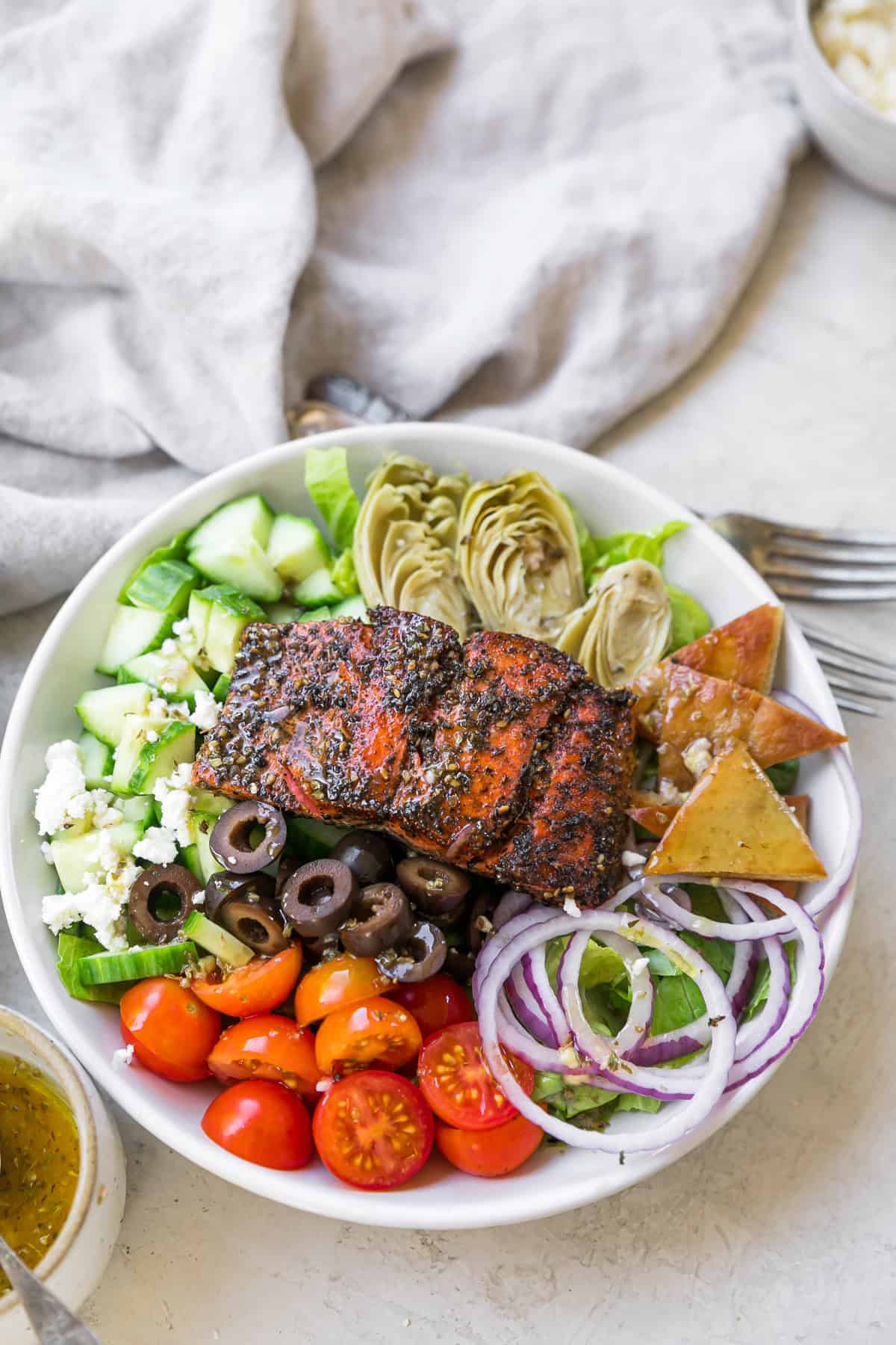 heavily seasoned greek salmon salad in bowl with pitas next to dressing and forks