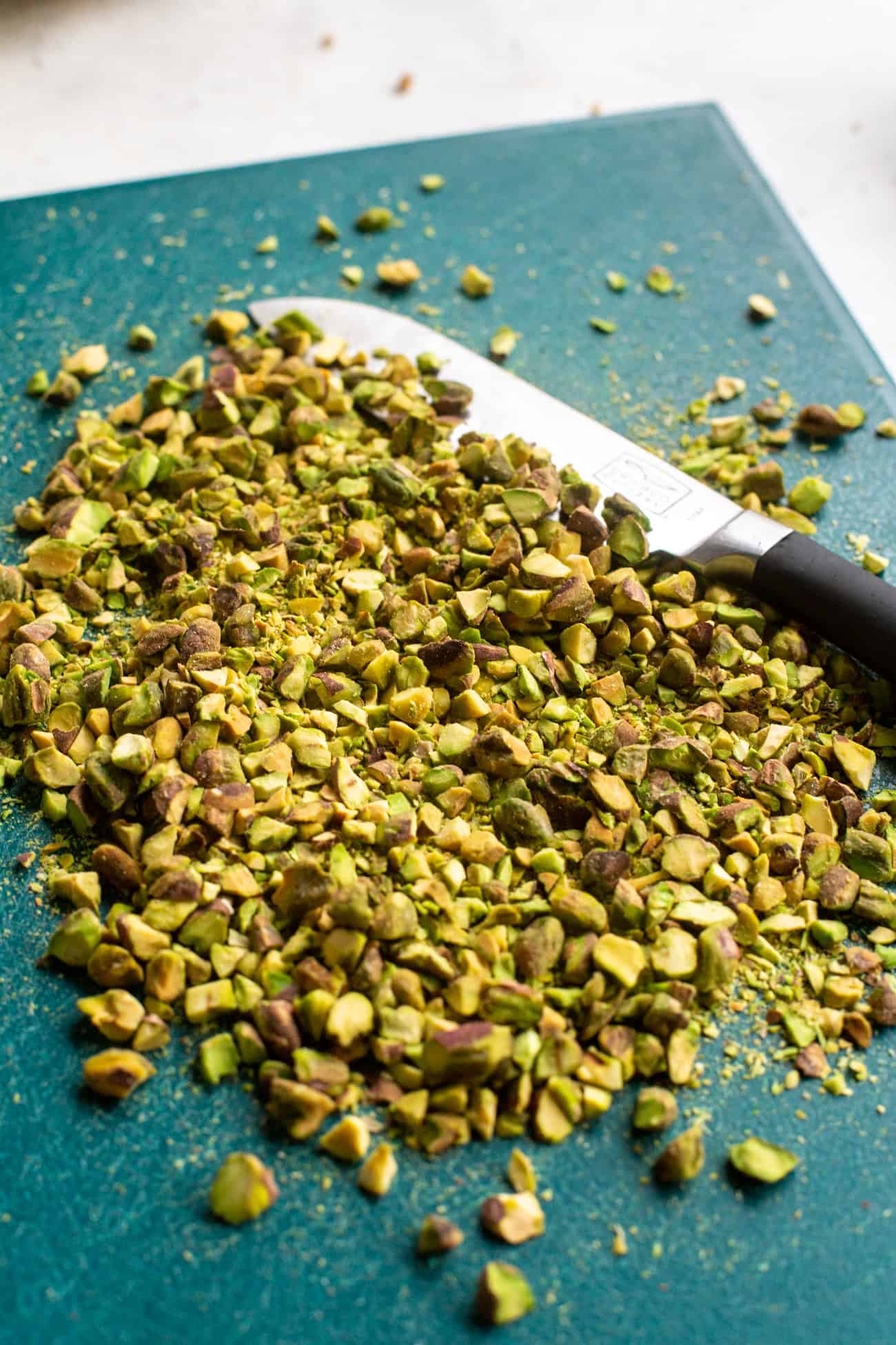 finely chopped crushed pistachios on teal cutting board.