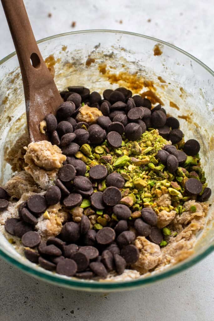 close up of chocolate chips and pistachios mixing into cookie dough.