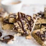 straight on image of square piece of peanut butter protein bars on white paper with wooden board.