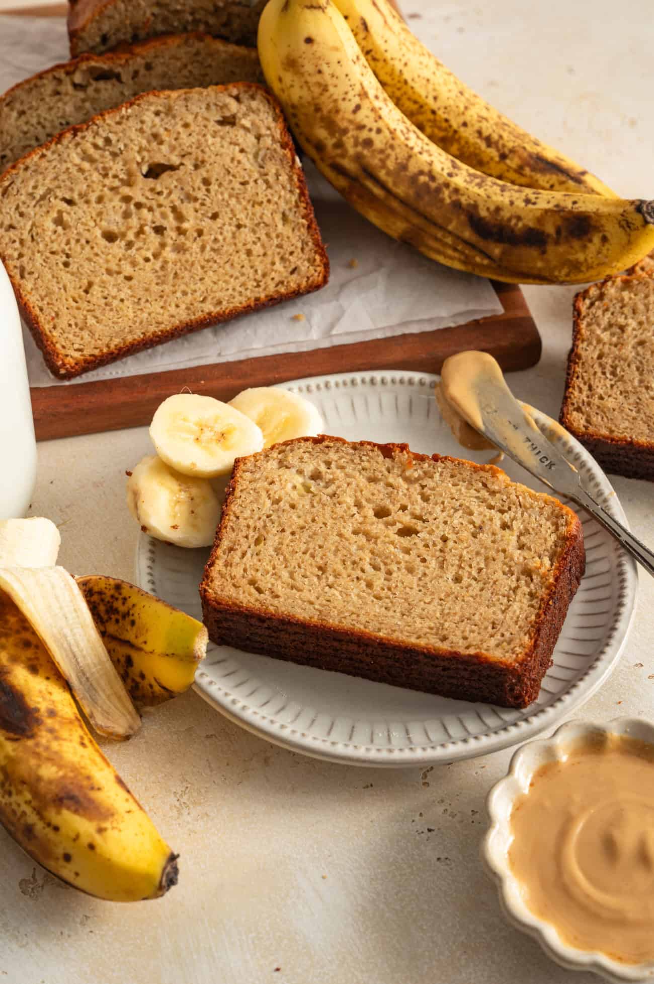 slice of banana bread on plate next to banana slices and banana bread loaf.