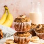 two healthy banana muffins stacked on top of each other with milk and bananas in background.