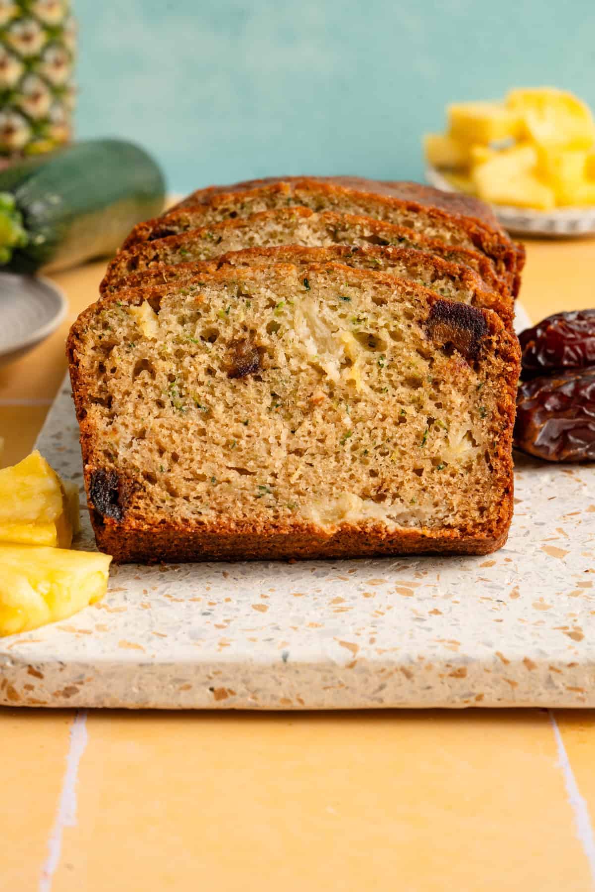 Zucchini bread recipe with pineapple on yellow tile with turquoise background.