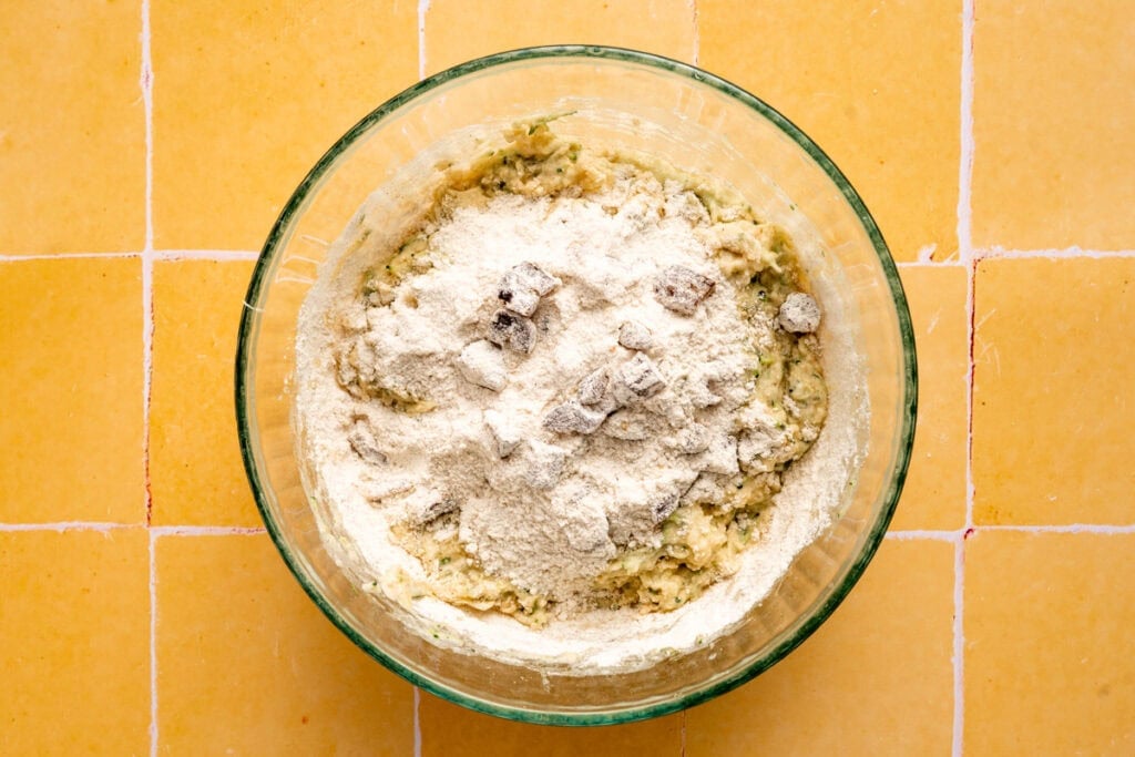 dry ingredients mixed with wet ingredients in glass bowl on yellow tile.