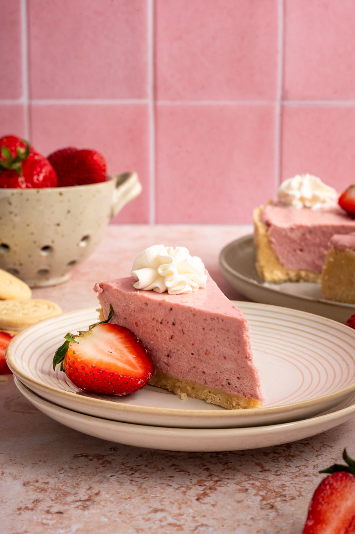 slice of no bake strawberry cheesecake on stacked plates with pink tile background.