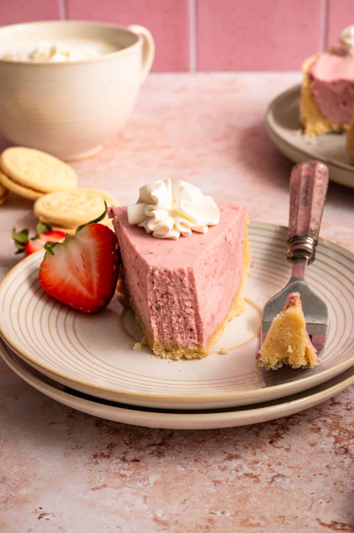 straight on view of bite with fork of no bake strawberry cheesecake on stacked plates.