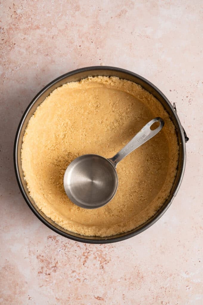 overhead view of no bake crust in springform pan with measuring cup.