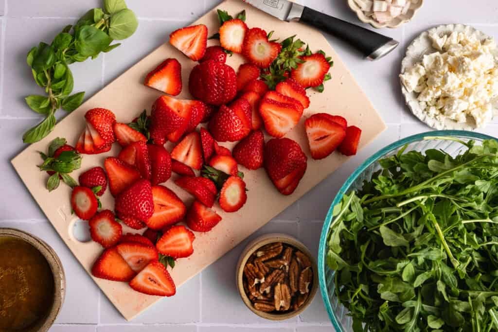 overhead view of strawberry arugula salad ingredients on gray tile board.