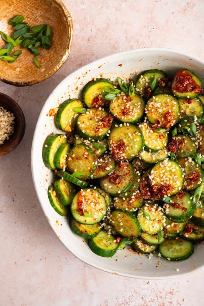 overhead view of chili crisp oil on sliced cucumbers and white sesame seeds.