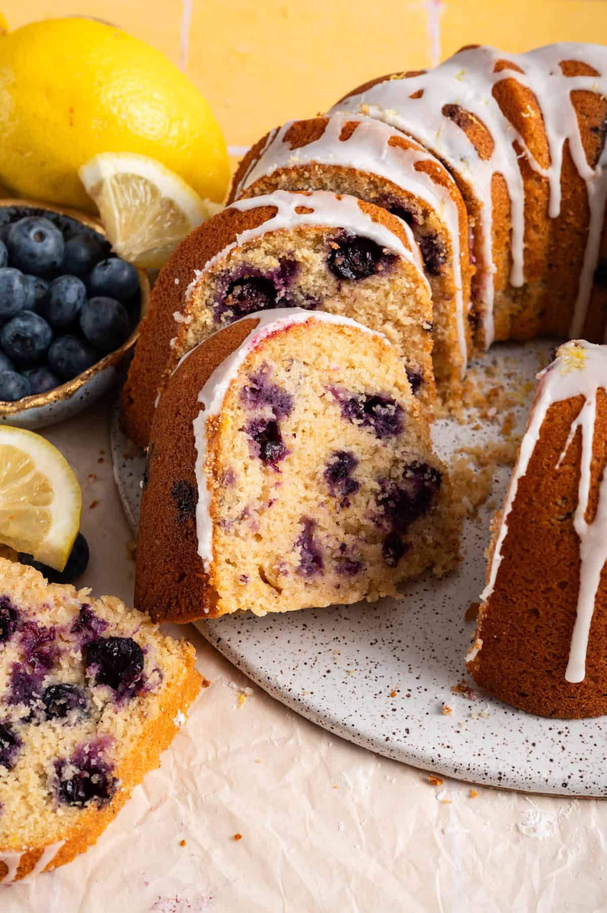lemon blueberry bundt cake sliced on serving tray next to fresh blueberries and lemons.