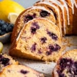 blueberry lemon bundt cake sliced on round platter next to blueberries and lemon in background.