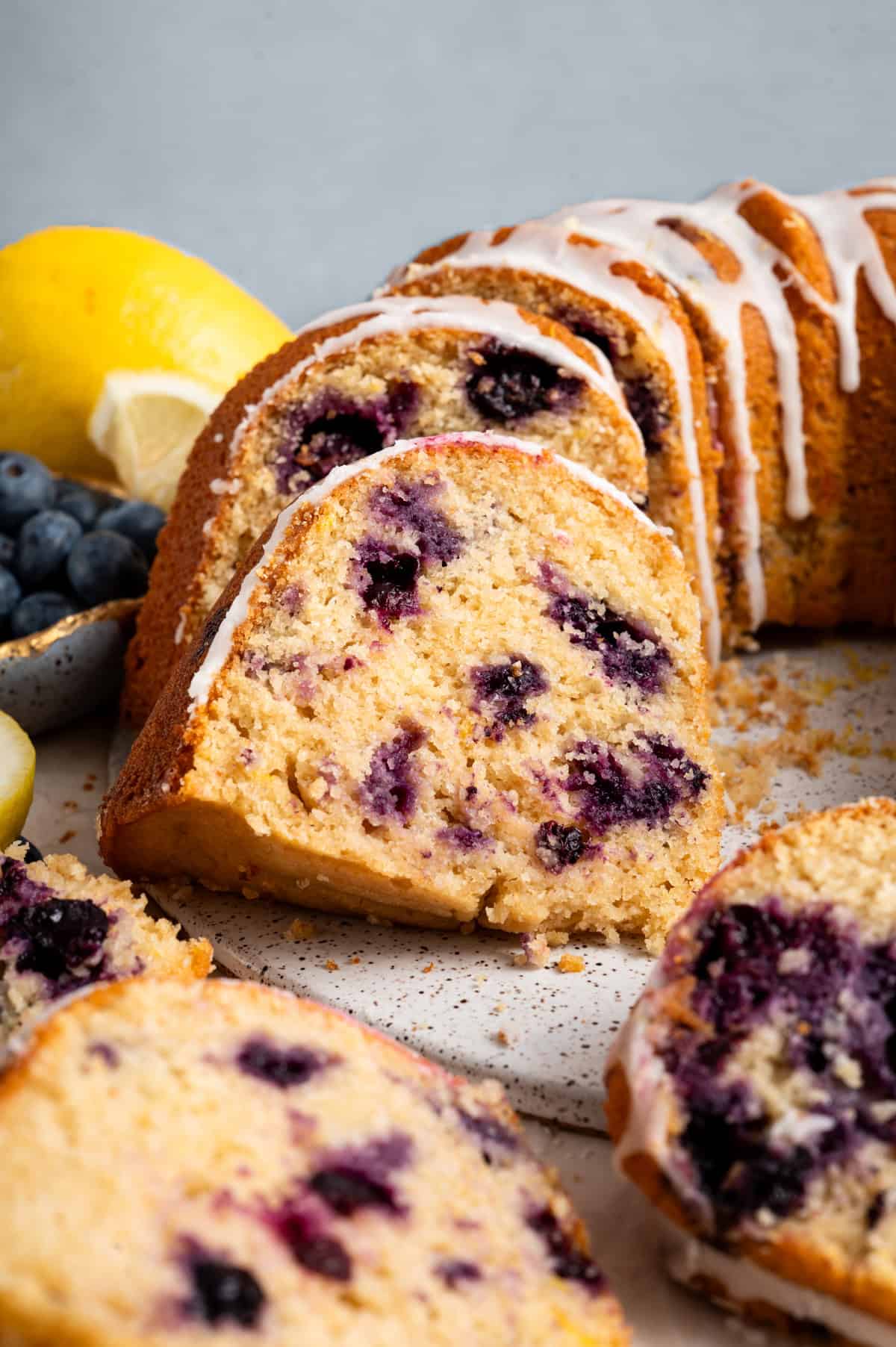 blueberry lemon bundt cake sliced on round platter next to blueberries and lemon in background.