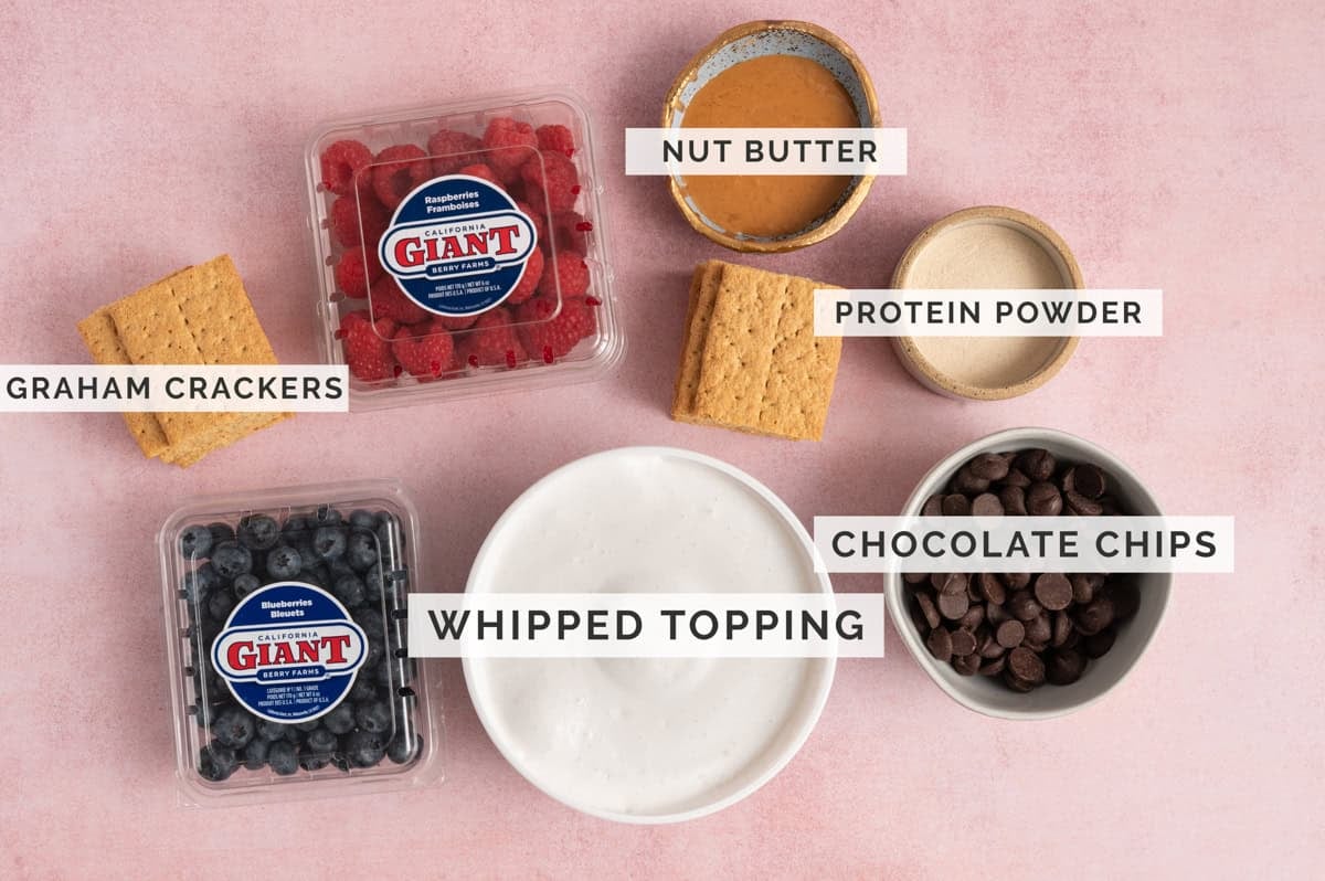 ingredients laid out on pink background, including berries and ingredients for frozen smores recipe.