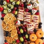 wooden board with healthy halloween snacks like chocolate covered berries, hand pies, spider waffles.