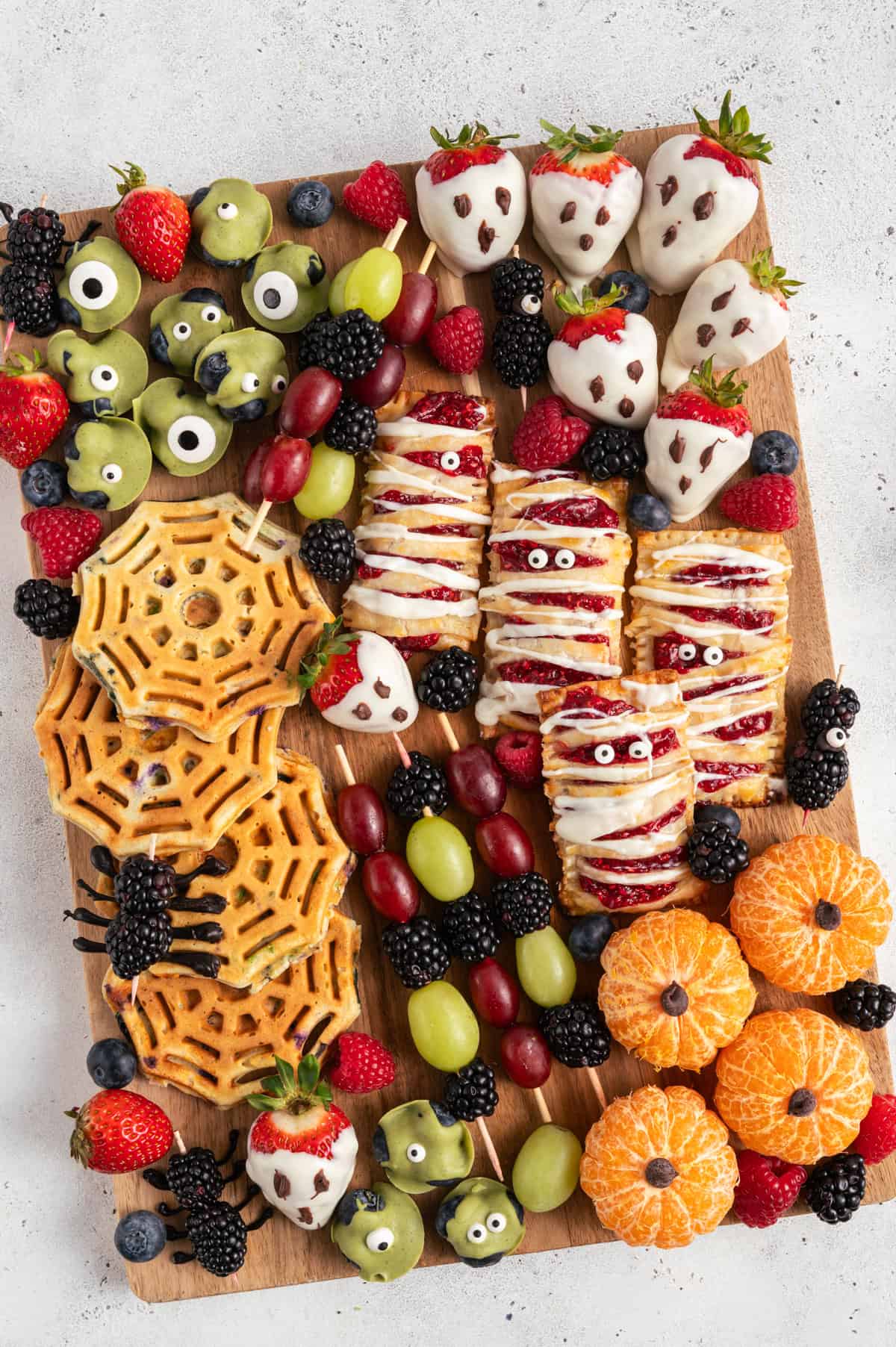 wooden board with healthy halloween snacks like chocolate covered berries, hand pies, spider waffles.